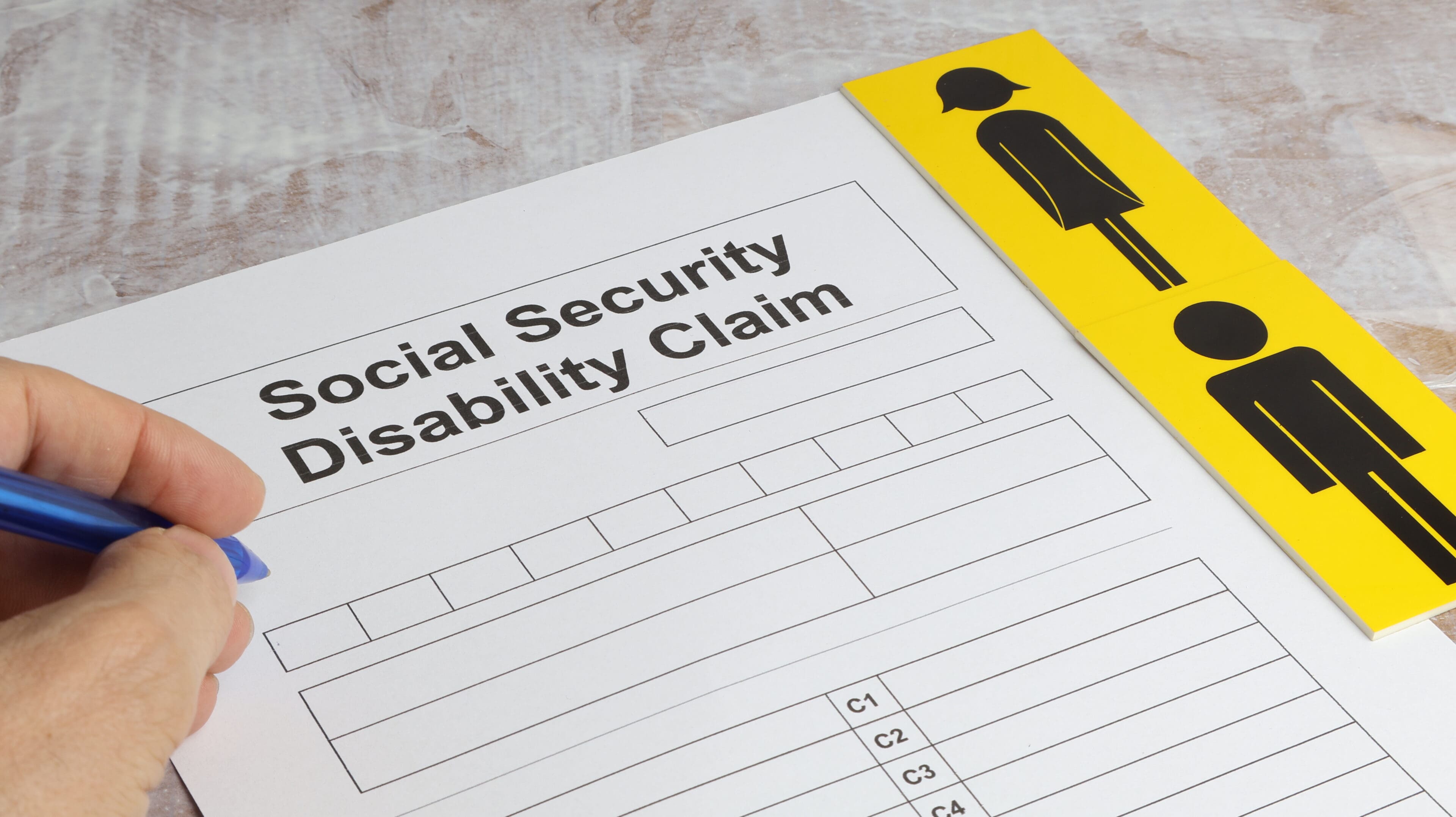 Disability claim form social security desk with man's hand writing.